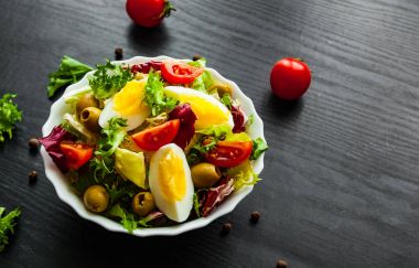 koyu ahşap arka plan üzerinde domates, yumurta ve zeytin kase ile çeşitli taze karışımı salata yaprakları