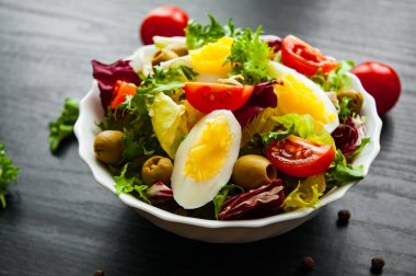 koyu ahşap arka plan üzerinde domates, yumurta ve zeytin kase ile çeşitli taze karışımı salata yaprakları