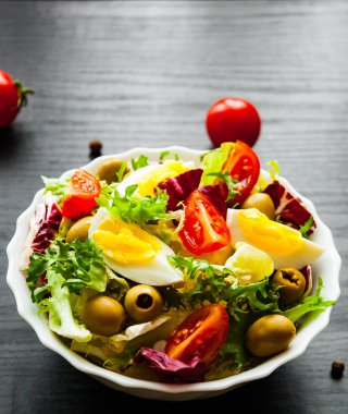 koyu ahşap arka plan üzerinde domates, yumurta ve zeytin kase ile çeşitli taze karışımı salata yaprakları
