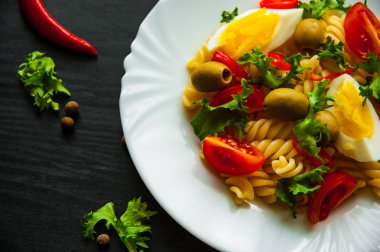 Düdük makarna salata domates, yumurta ve koyu ahşap arka plan üzerinde plaka zeytin ile