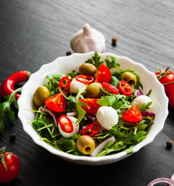 taze salata ile yeşil rucola, peynir, zeytin, domates, soğan, biber koyu ahşap arka plan üzerinde beyaz kase