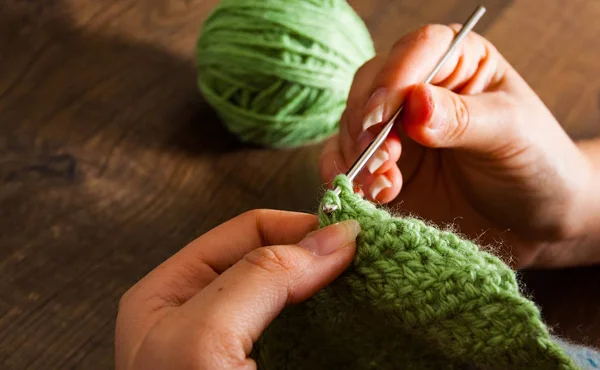 woman hands knitting with crochet hook on a wooden background