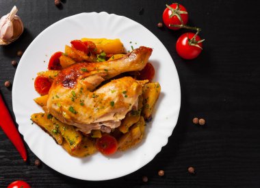 Kızarmış tavuk budu havuç, soğan ve patates ile koyu ahşap arka plan üzerinde beyaz bir tabakta servis