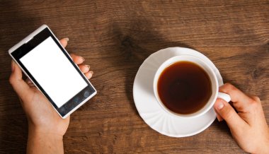 Cep telefonu ve fincan çay ahşap arka plan üzerinde eller. Üstten Görünüm