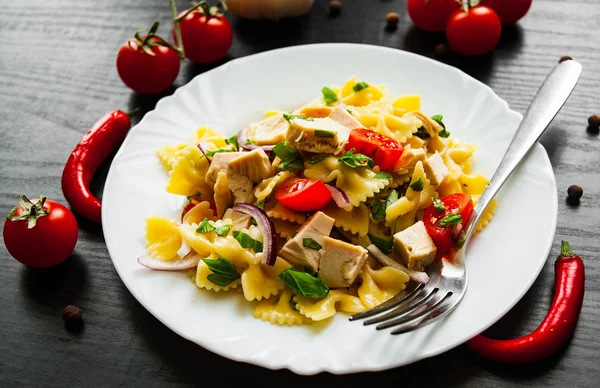 farfalle pasta salad with chicken and vegetables in plate on dark wooden background