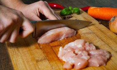 Aşçı Şef eller kadın çiğ tavuk göğsü bir ahşap arka plan üzerinde keser..