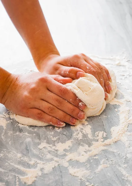 Woman\'s hands knead dough on wooden table