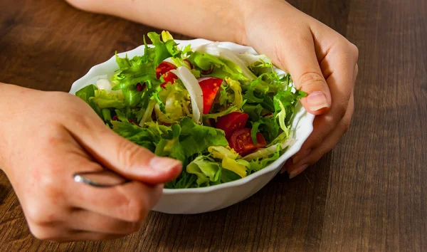 Çatal üzerinde ahşap arka plan kase domates ile çeşitli taze karışımı salata tutan kadın el yakın çekim yaprak 