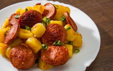 Kavrulmuş patates ve ahşap masa üzerinde beyaz tabak sosis