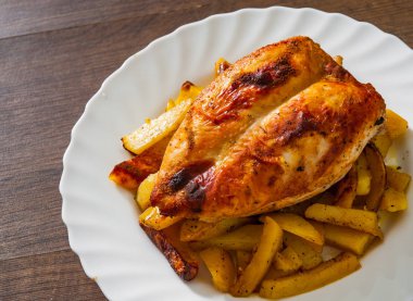 ahşap masa üzerinde bir tabak patates ile kavrulmuş tavuk göğsü