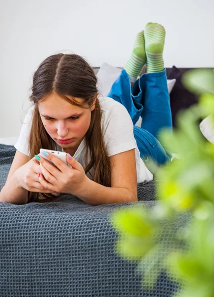 ティーンエイ ジャーの女の子が自宅のベッドの上に敷設のスマート フォンで楽しい時を過す — ストック写真