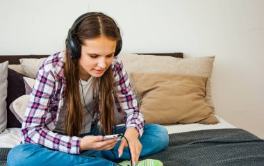 Kulaklık ve odada müzik dinlerken holding akıllı telefon kullanan genç kız