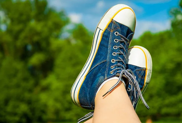 Female feet in jeans sneakers on the background of a sky and tree sunny summer day