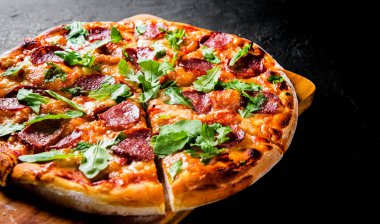 Mozzarella peyniri, salam, domates sos, biber, baharat ve taze roka ile biberli Pizza. İtalyan pizza koyu gri siyah arduvaz arka plan üzerinde