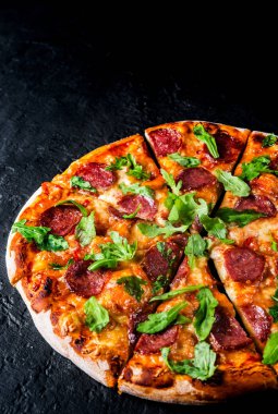 Mozzarella peyniri, salam, domates sos, biber, baharat ve taze roka ile biberli Pizza. İtalyan pizza koyu gri siyah arduvaz arka plan üzerinde
