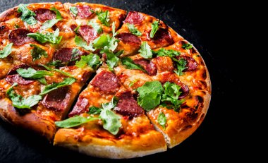 Mozzarella peyniri, salam, domates sos, biber, baharat ve taze roka ile biberli Pizza. İtalyan pizza koyu gri siyah arduvaz arka plan üzerinde