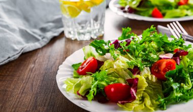 Tahta arka planda beyaz tabakta domatesli çeşitli taze salata yaprakları..