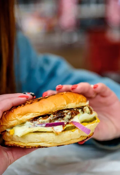 Woman hand is holding a fresh burger before eating on street cafe