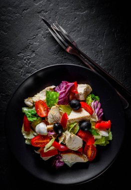 Taze salata ile tavuk göğsü, peynir, siyah zeytin, kırmızı biber, marul, taze salata ve domates siyah bir tabakta siyah siyah kayrak zemin üzerinde