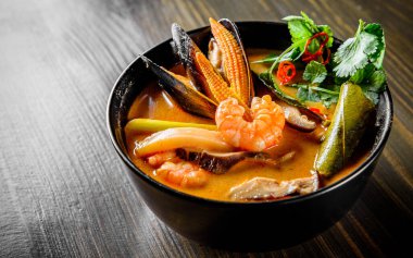 Tava Asya yemeği. Tom Yam çorbası ahşap masa arkasında siyah kasede