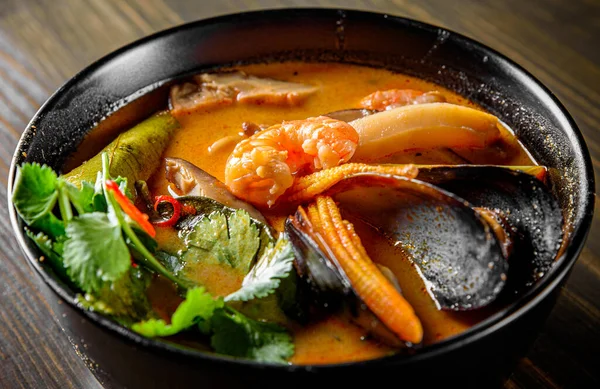 pan asian food. Tom Yam soup in black bowl on wooden table background