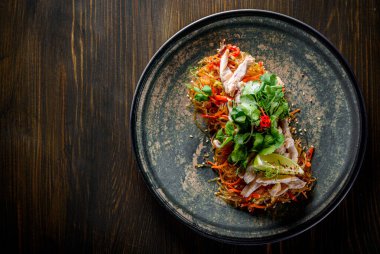 Tavuk etli, sebzeli ve ahşap masa arkasında susamlı Udon kızartmalı erişte.