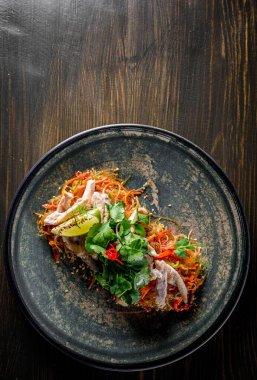 Tavuk etli, sebzeli ve ahşap masa arkasında susamlı Udon kızartmalı erişte.