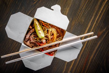 Biftek, sebze ve karton kutuda ahşap masa arkasında susamlı Udon kızartmalı erişte.