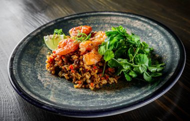 Kızarmış pirinç, karides ve sebzeler ahşap masa arkasında.