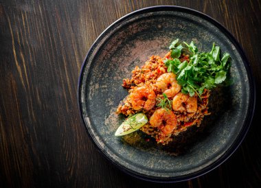 Kızarmış pirinç, karides ve sebzeler ahşap masa arkasında.