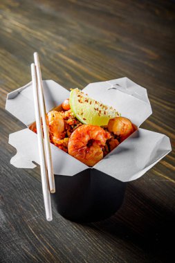 Kızarmış pirinç, karides ve sebzeler ahşap masa arkasında karton kutuda.