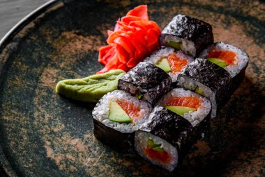 Somon balıklı suşi, avokado, siyah ahşap masa arka planında pirinç.