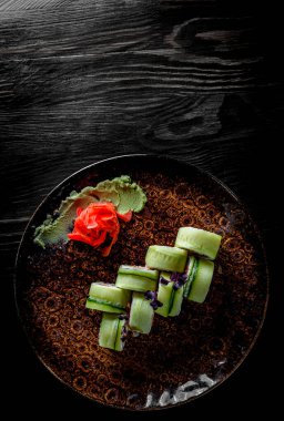  Ton balıklı suşi rulosu, salatalık, krem peynir, siyah ahşap masa arkasında tabakta pirinç.