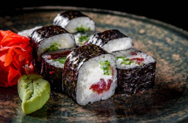 Ton balıklı suşi rulosu, salatalık, krem peynir, siyah ahşap masa arkasında tabakta pirinç.