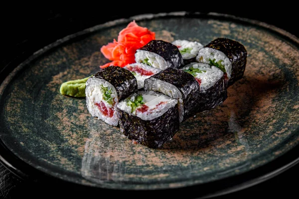 sushi roll with tuna, cucumber, cream cheese, rice in plate on black wooden table background