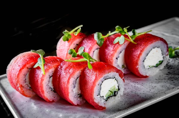 sushi roll with tuna, cream cheese, cucumber, rice in plate on black wooden table background