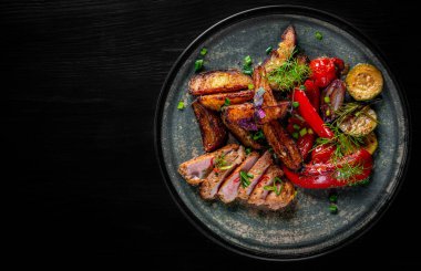 Patatesli kızarmış et, biber, domates, otlar ve baharatlar siyah ahşap masa arkasında.