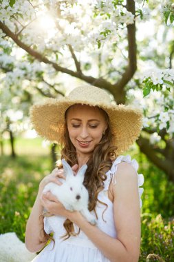 Çiçek açan elma bahçesinde beyaz tavşanlı güzel kız.
