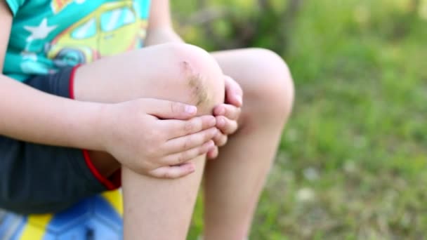El niño sostiene la herida en su rodilla . — Vídeos de Stock