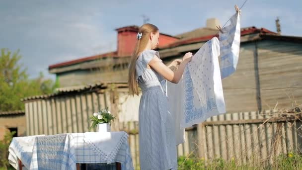 Mulher loira aldeão pendurado molhado branco-azul lavanderia no varal no quintal — Vídeo de Stock