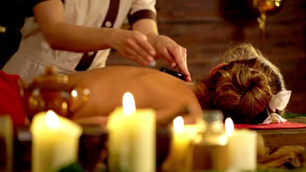 Terapia LaStone masaż w salonie spa. Na pierwszym planie są płonące świece. 4K — Wideo stockowe