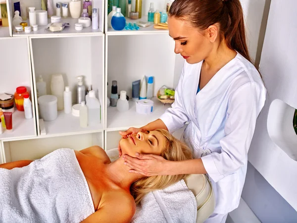 Mujer de mediana edad tomar masaje facial en salón botellas de cosméticos . —  Fotos de Stock