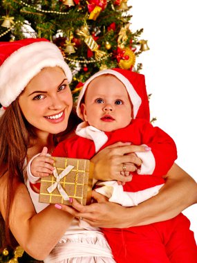 Anne giyen Santa şapka holding bebek Noel ağacı altında.