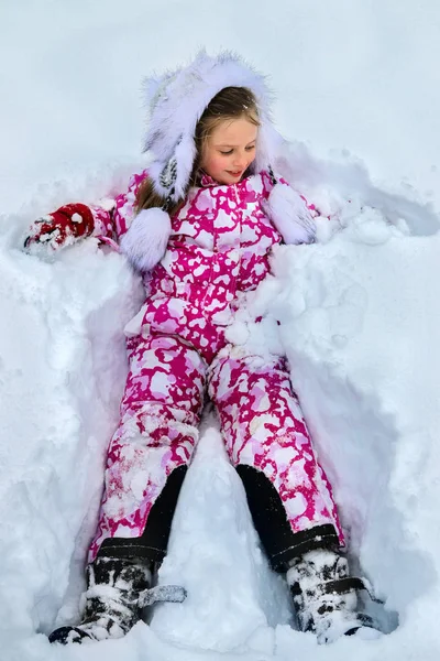 Menina criança vestindo roupas de inverno deitado na neve  . — Fotografia de Stock