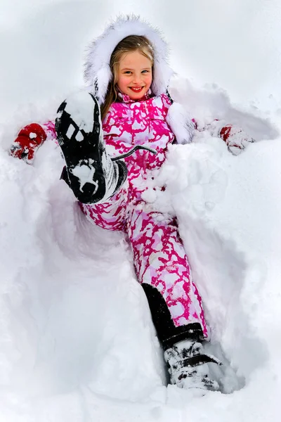 Little girl wearing winter clothes lying in deep snow . — Stock Photo, Image