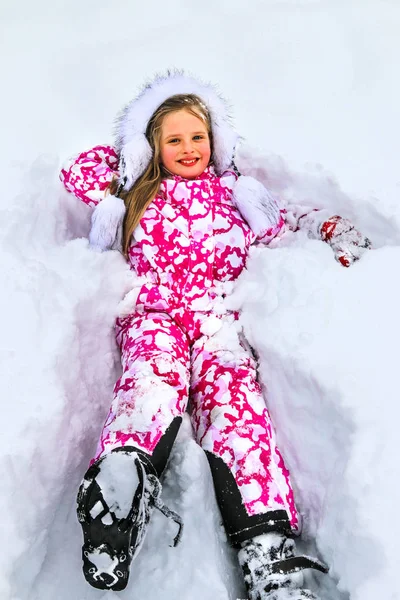 A criança, uma menina deitada na neve e rindo . — Fotografia de Stock
