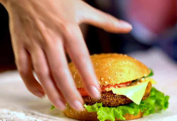 Hamburguesa de comida rápida en tablero de madera. La mano humana tomar hamburguesa con queso . —  Fotos de Stock