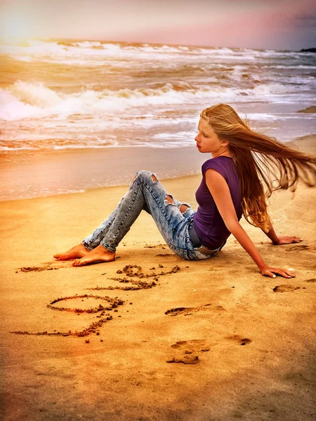 Frau am Strand bei Sonnenuntergang schreibt Liebe auf Sand. — Stockfoto