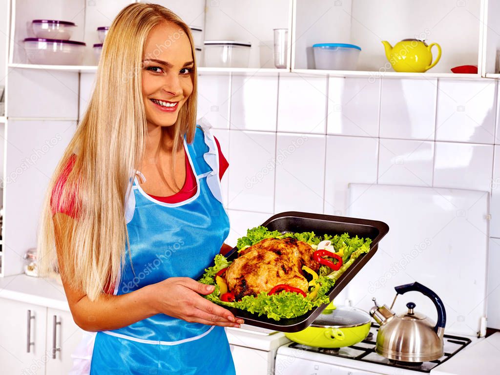 Women in kitchen is cooking roast meat food in oven.