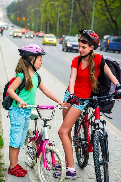 Niñas niños ciclismo en carril bici amarillo. Hay coches en la carretera. . — Foto de Stock